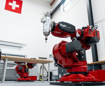 Roter CNC-Fräsroboter von MABI Robotics mit integrierter Frässpindel in einer Produktionshalle. Im Hintergrund steht ein weiterer Industrieroboter.